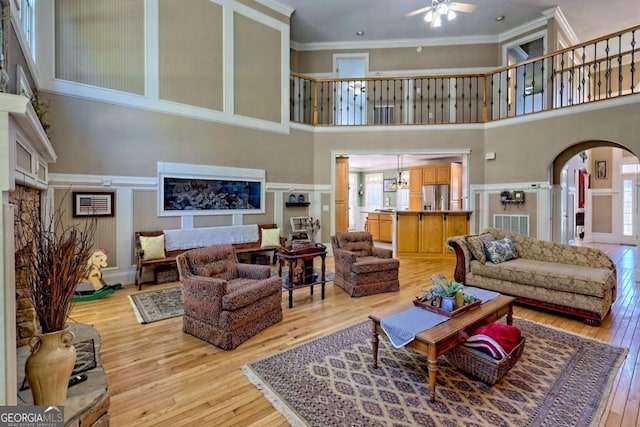 living room featuring arched walkways, light wood-style floors, crown molding, a decorative wall, and ceiling fan