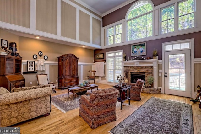 living room with a towering ceiling, a fireplace, wood finished floors, and crown molding