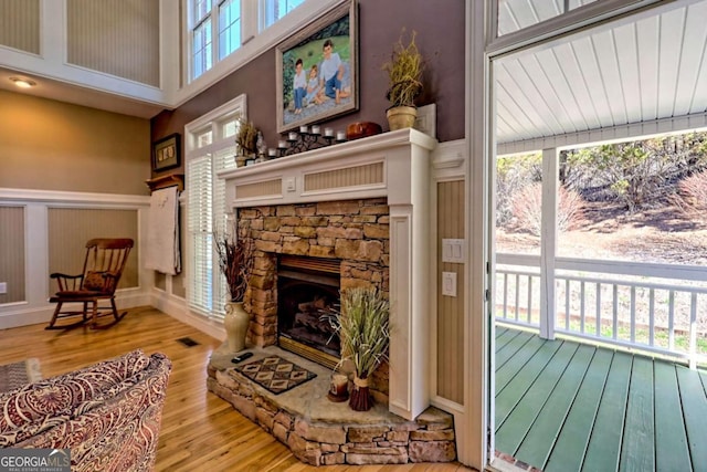 living area with a stone fireplace, wainscoting, a decorative wall, and wood finished floors