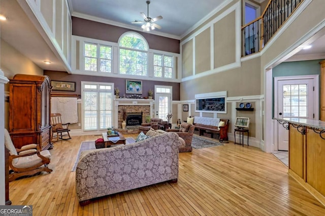 living area with crown molding, ceiling fan, a stone fireplace, light wood-style flooring, and a towering ceiling