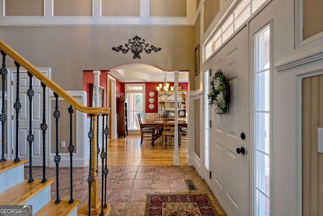 tiled entrance foyer with visible vents, stairway, arched walkways, a towering ceiling, and ornate columns