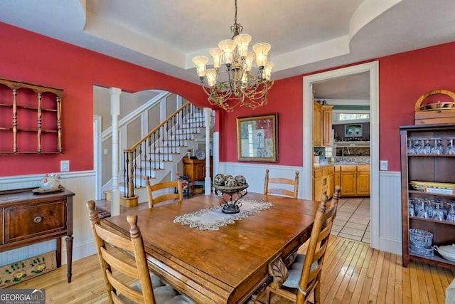 dining area featuring a wainscoted wall, a raised ceiling, light wood-style flooring, and stairway