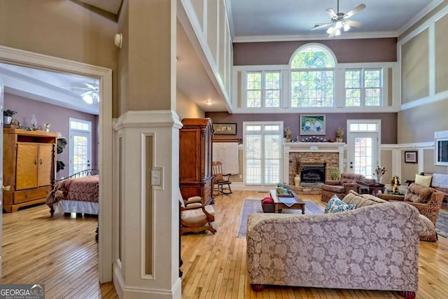 living area with a stone fireplace, ceiling fan, a towering ceiling, and a healthy amount of sunlight