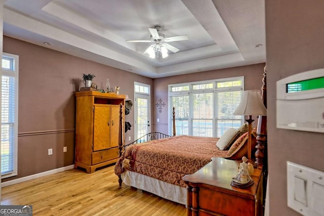 bedroom featuring a tray ceiling, baseboards, and light wood finished floors