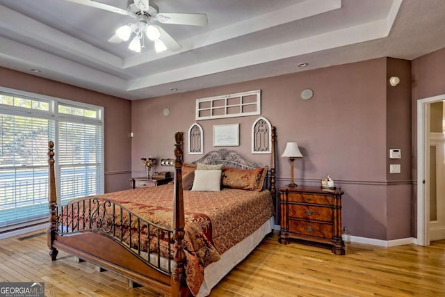 bedroom with ceiling fan, baseboards, a raised ceiling, and light wood-style floors