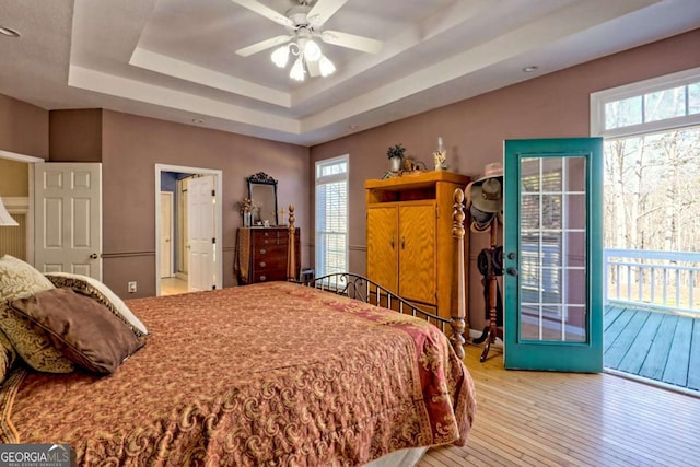 bedroom with access to exterior, a tray ceiling, and hardwood / wood-style flooring