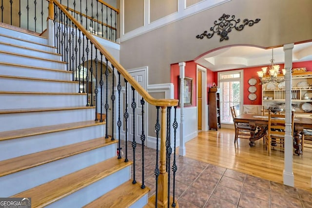 staircase with a tray ceiling, arched walkways, a high ceiling, tile patterned flooring, and decorative columns