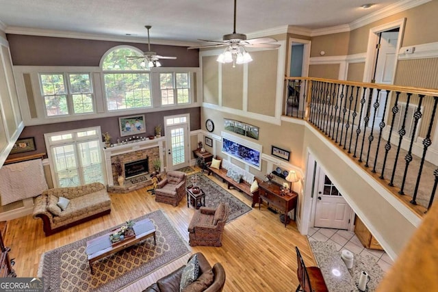 living room featuring a stone fireplace, crown molding, wood finished floors, and ceiling fan