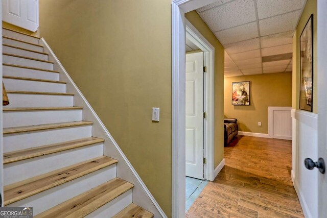 stairway featuring baseboards, a paneled ceiling, and wood finished floors