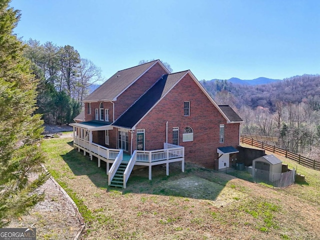 back of property with a deck with mountain view, fence, a yard, a wooded view, and brick siding