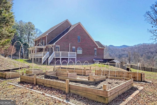 back of property featuring a garden, fence, brick siding, and a wooden deck