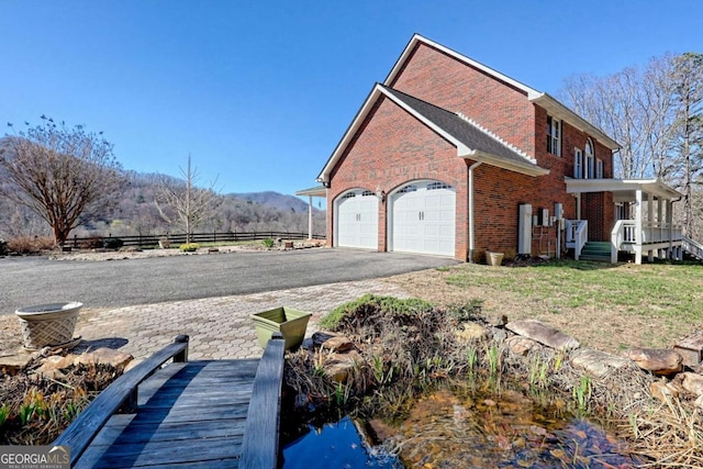 view of home's exterior featuring aphalt driveway, a mountain view, covered porch, a garage, and brick siding