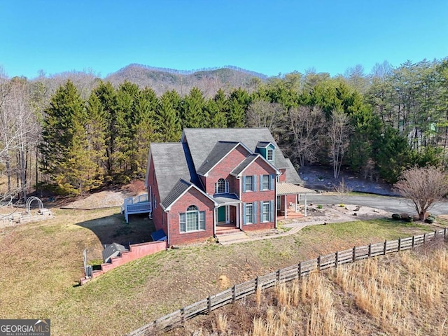 view of front of property with a view of trees, brick siding, a front yard, and fence