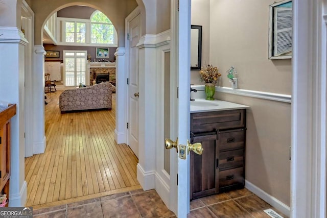 bathroom with a stone fireplace, vanity, visible vents, and hardwood / wood-style floors