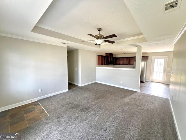 unfurnished living room with visible vents, ornamental molding, a ceiling fan, a tray ceiling, and dark carpet