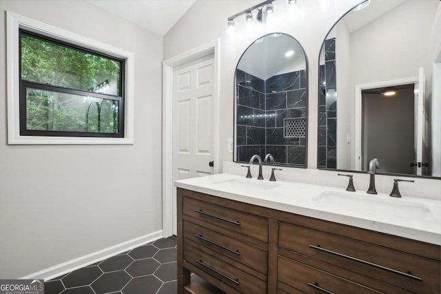 full bath featuring double vanity, vaulted ceiling, baseboards, and a sink