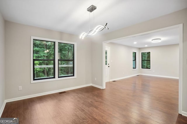 spare room featuring a healthy amount of sunlight, visible vents, dark wood-style flooring, and baseboards