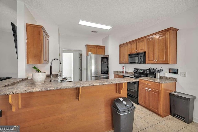 kitchen featuring a peninsula, light tile patterned flooring, black appliances, a kitchen bar, and brown cabinets