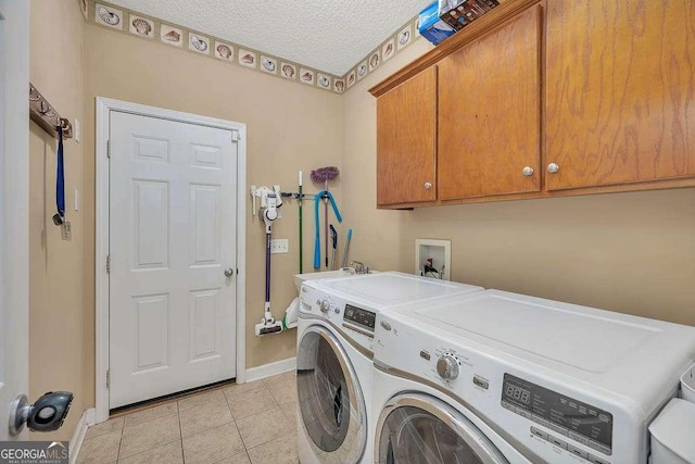 laundry area with washer and clothes dryer, a textured ceiling, cabinet space, light tile patterned floors, and baseboards