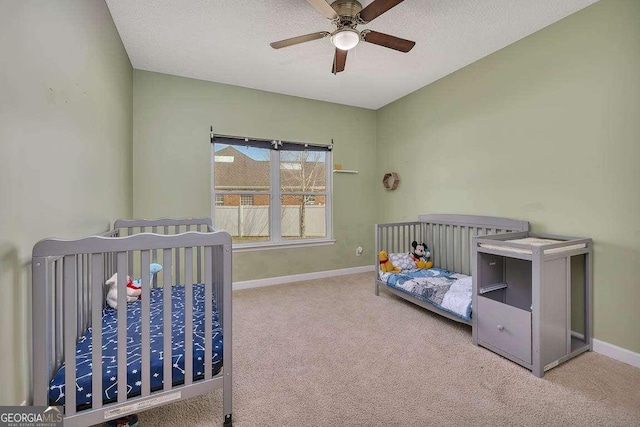 carpeted bedroom with a textured ceiling, a crib, and baseboards