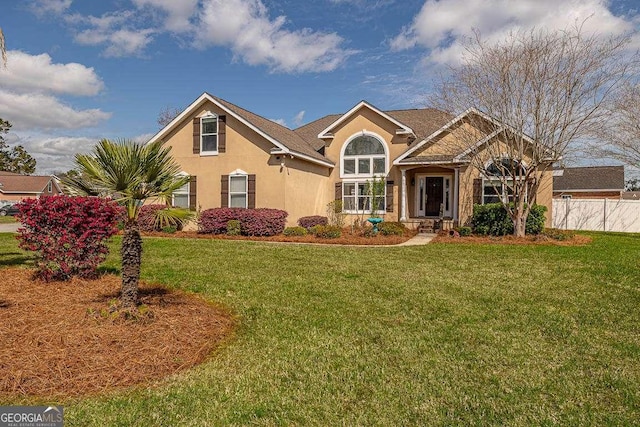 view of front of house featuring stucco siding, a front yard, and fence