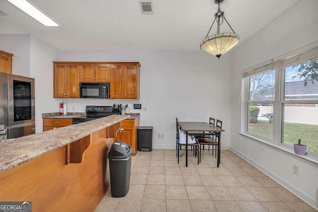 kitchen featuring visible vents, decorative light fixtures, light tile patterned floors, brown cabinets, and black appliances