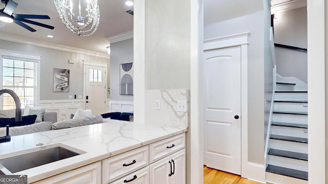 kitchen featuring ceiling fan with notable chandelier, ornamental molding, light stone countertops, and a sink