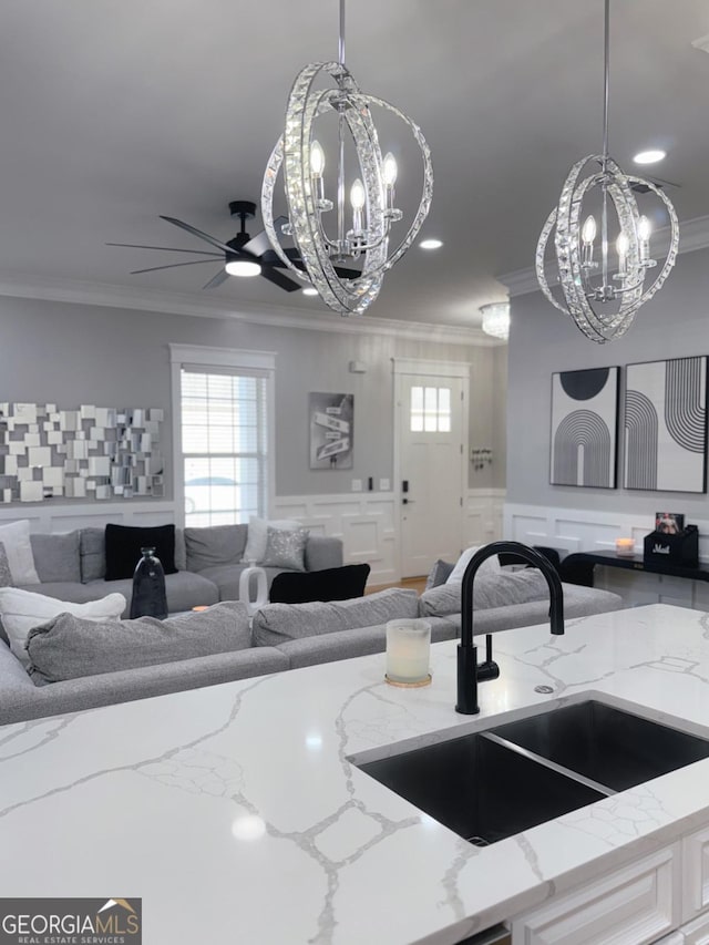 kitchen with a wainscoted wall, ornamental molding, a sink, decorative light fixtures, and open floor plan