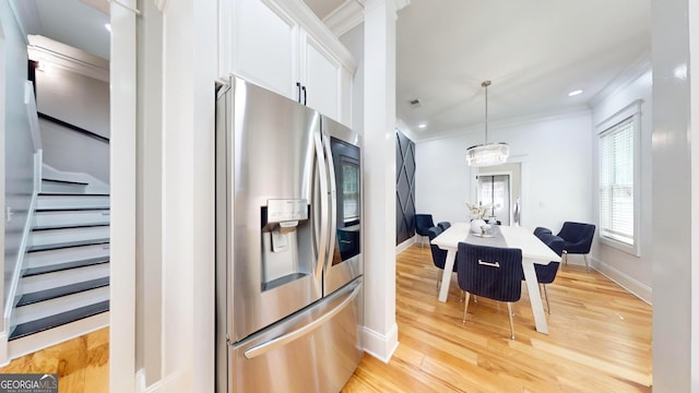 kitchen with ornamental molding, stainless steel refrigerator with ice dispenser, light wood-style floors, white cabinets, and baseboards