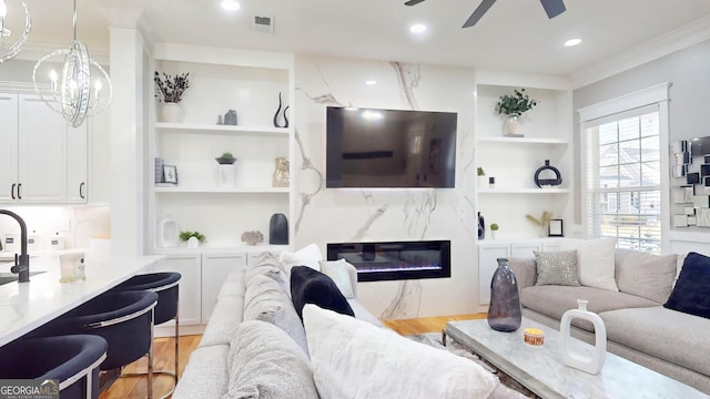 living room featuring built in shelves, a ceiling fan, a fireplace, and light wood finished floors