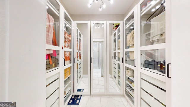 spacious closet featuring marble finish floor and a chandelier