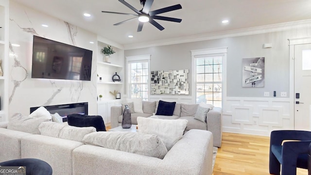 living area featuring a ceiling fan, light wood finished floors, recessed lighting, ornamental molding, and a decorative wall