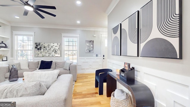 living area with ceiling fan, light wood finished floors, a wealth of natural light, and ornamental molding