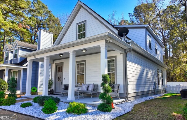 view of front facade with central AC unit, covered porch, and fence