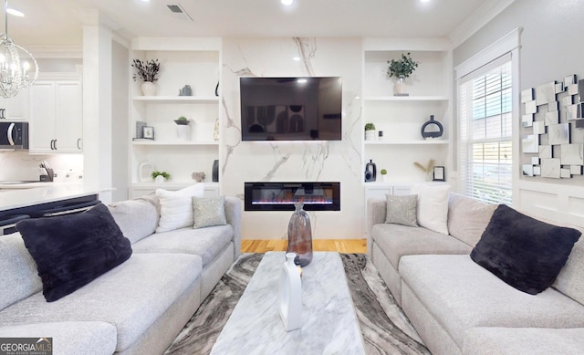 living room featuring visible vents, built in shelves, ornamental molding, a premium fireplace, and wood finished floors