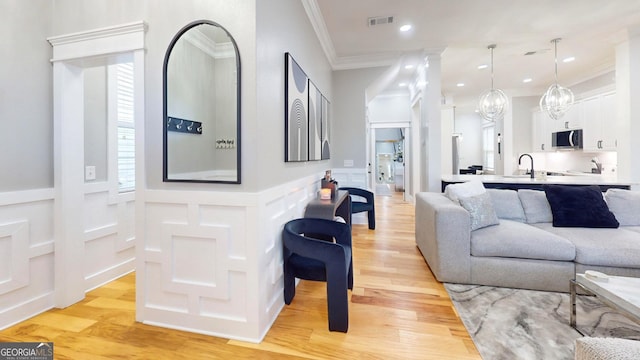 living room featuring visible vents, light wood-style flooring, wainscoting, crown molding, and a decorative wall