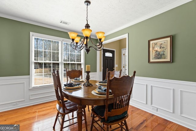 dining area with a wainscoted wall, visible vents, light wood finished floors, a textured ceiling, and a chandelier