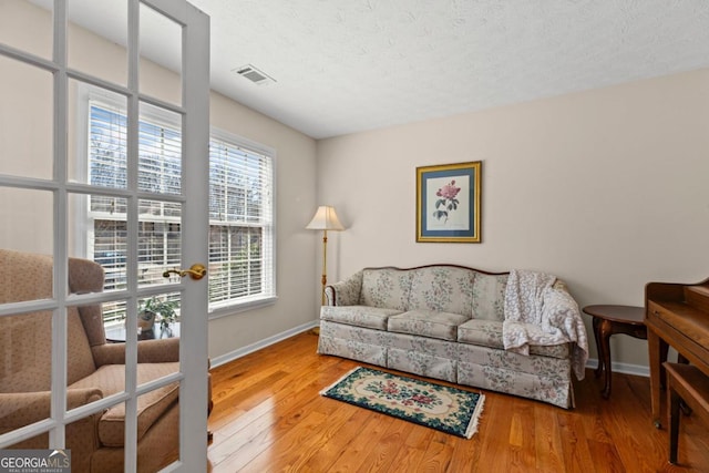 living area with a textured ceiling, wood finished floors, visible vents, and baseboards