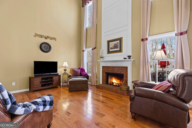 living room featuring hardwood / wood-style floors, a high ceiling, a fireplace, and baseboards