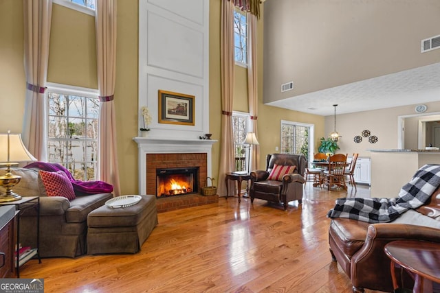 living area featuring a brick fireplace, plenty of natural light, visible vents, and light wood finished floors