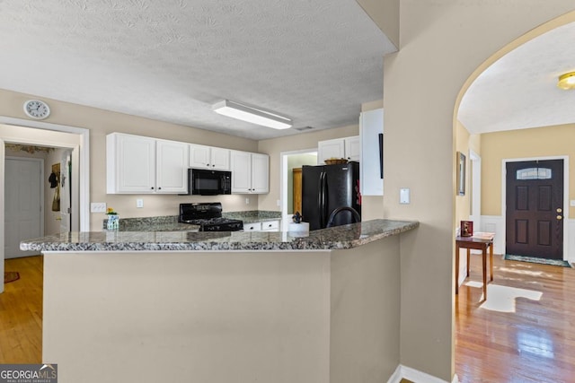 kitchen featuring dark stone counters, arched walkways, black appliances, and light wood finished floors