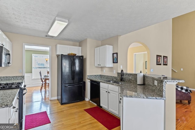 kitchen with a peninsula, arched walkways, white cabinets, black appliances, and a sink