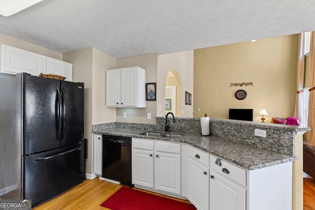 kitchen with light wood-type flooring, black appliances, a sink, a peninsula, and white cabinets