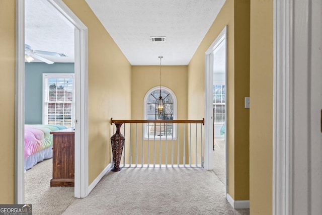 hallway with visible vents, a textured ceiling, carpet flooring, baseboards, and a chandelier