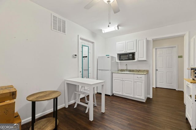 kitchen featuring visible vents, black microwave, freestanding refrigerator, white cabinetry, and a sink