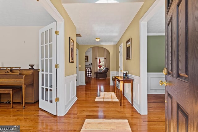 foyer featuring light wood-type flooring, arched walkways, visible vents, and wainscoting