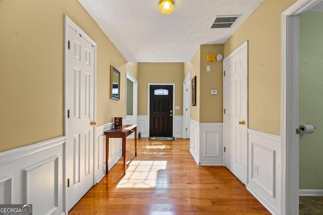 entrance foyer with a wainscoted wall, light wood-style floors, visible vents, and a textured ceiling