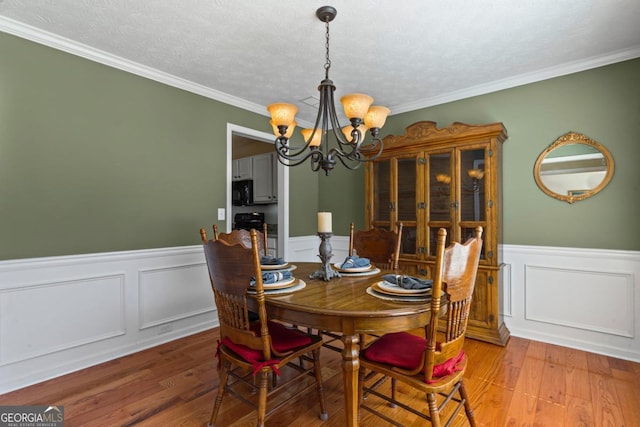 dining room featuring a textured ceiling, a notable chandelier, wainscoting, and light wood finished floors