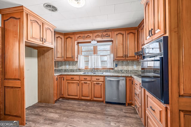 kitchen featuring oven, visible vents, brown cabinets, a sink, and stainless steel dishwasher