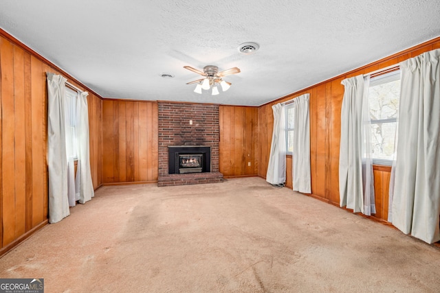 unfurnished living room with wooden walls, visible vents, light colored carpet, a fireplace, and a ceiling fan